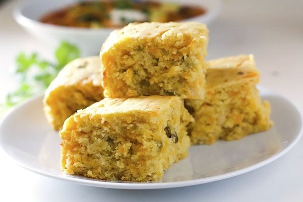 Close up picture of 4 pieces of cheesy green chile cornbread on a white plate. 