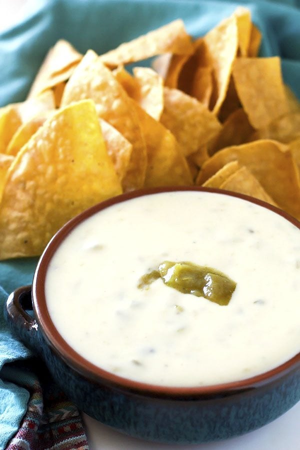 A bowl filled with queso dip that is surrounded by tortilla chips.