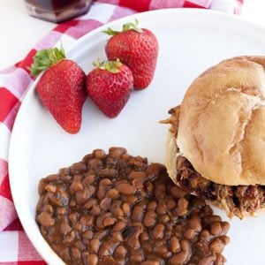 A plate full of Boston Baked Beans with some sandwiches and a Pulled Pork Sandwich. 