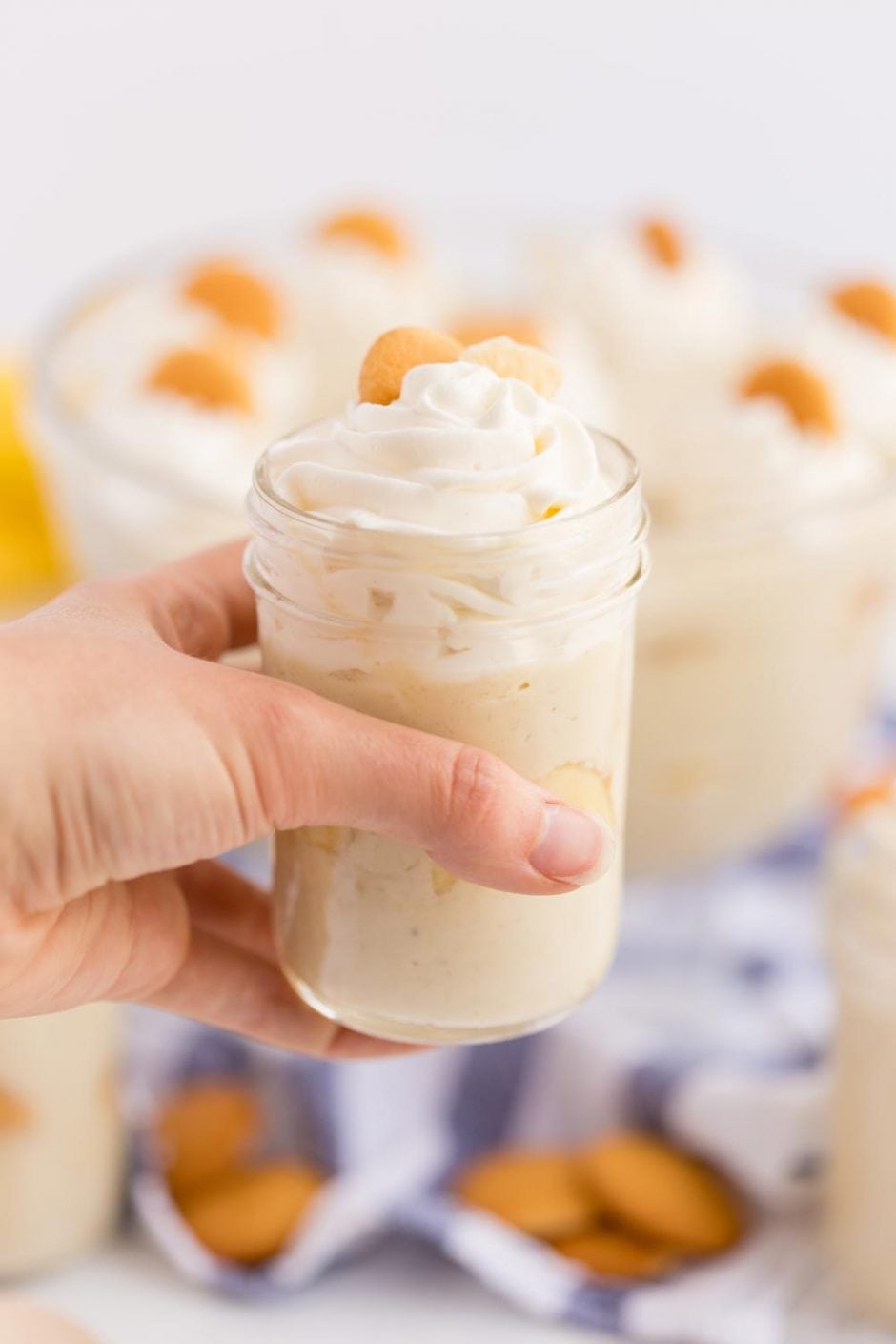 Banna pudding scooped into a mason jar topped with whipped cream, a slice of banana and a vanilla wafer.