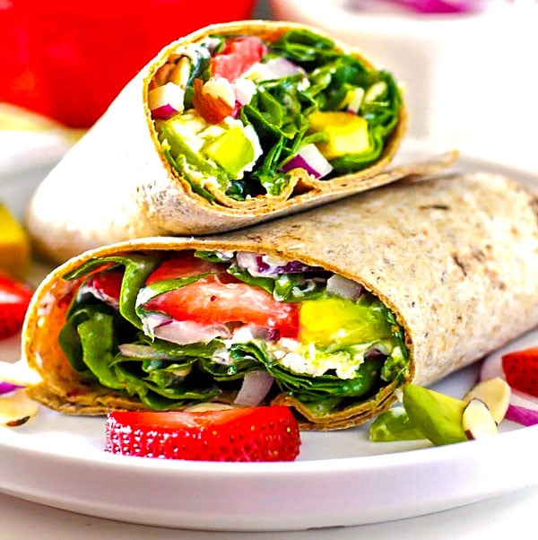 Strawberry Spinach Wraps on a white plate with strawberries, avocado, almonds, and red onions sprinkled around it.