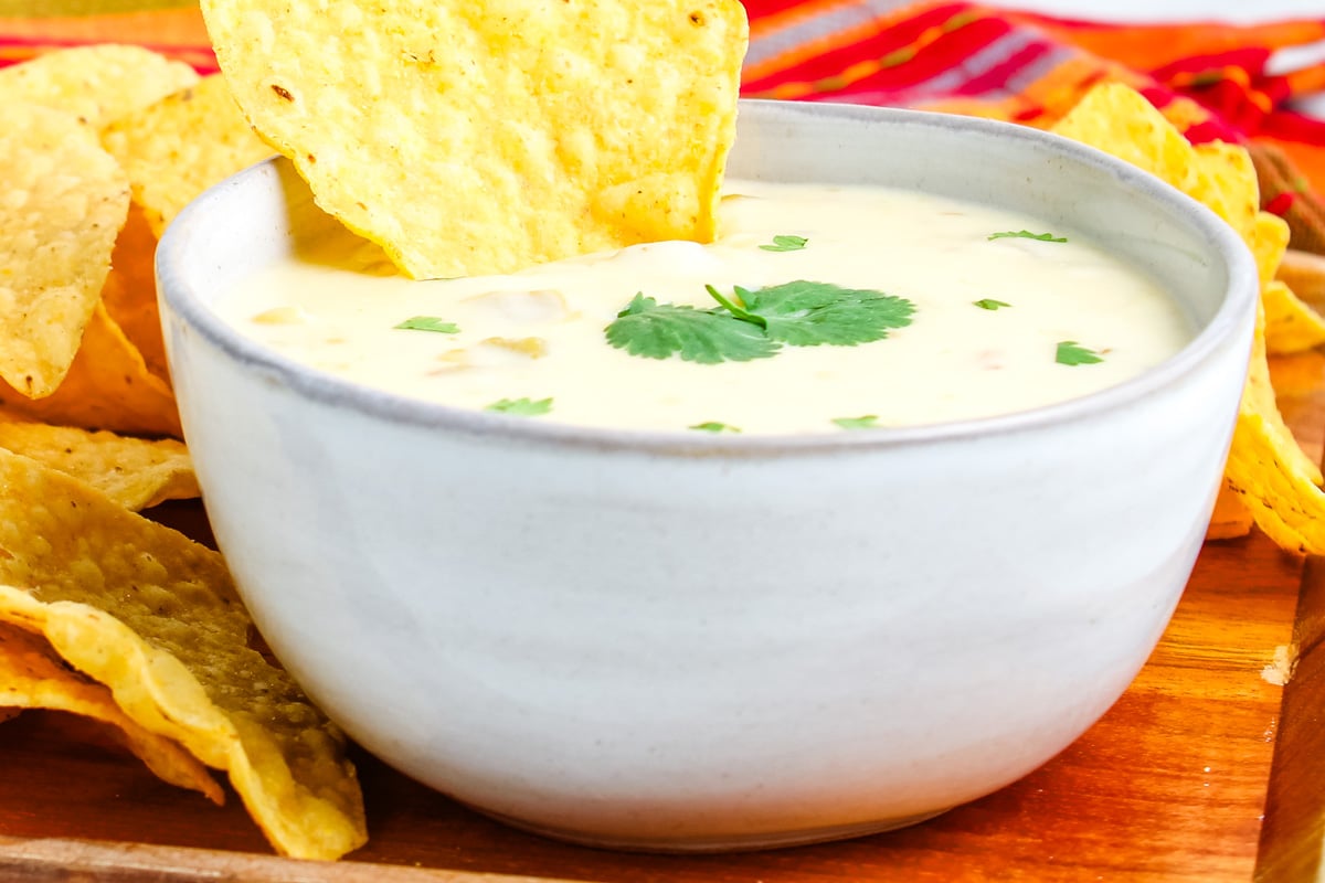 Green chile queso dip in a bowl with tortilla chips for dipping.