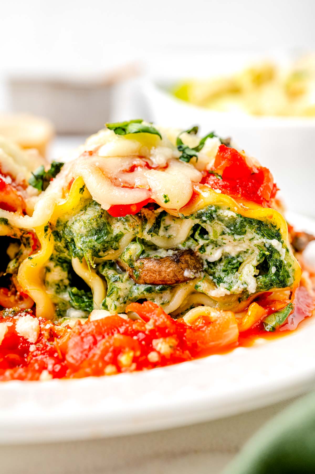 A close up picture of a Spinach Lasagna Roll on a white plate with sauce.