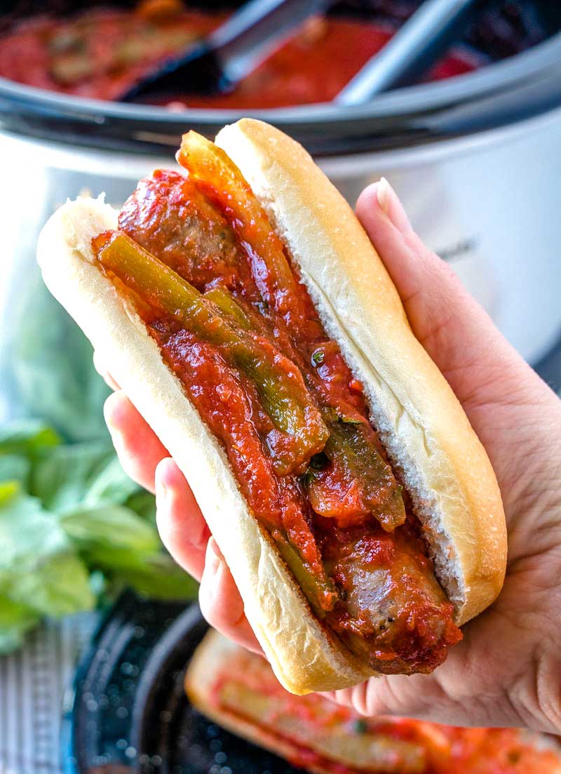 A hand picking up sausage and peppers on an Italian sub. 