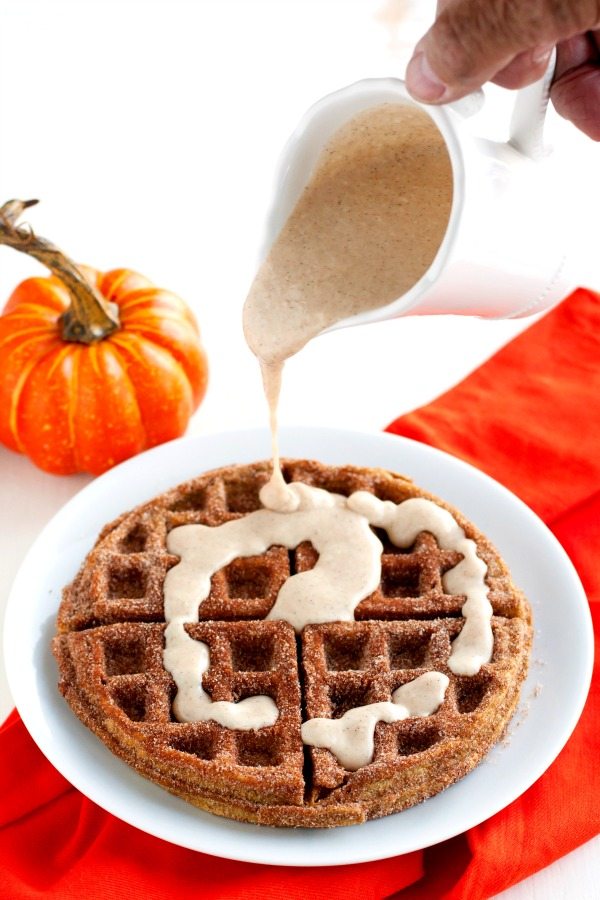 Pumpkin Churro Waffle on a plate with Spiced Cream Cheese glaze being drizzled on top