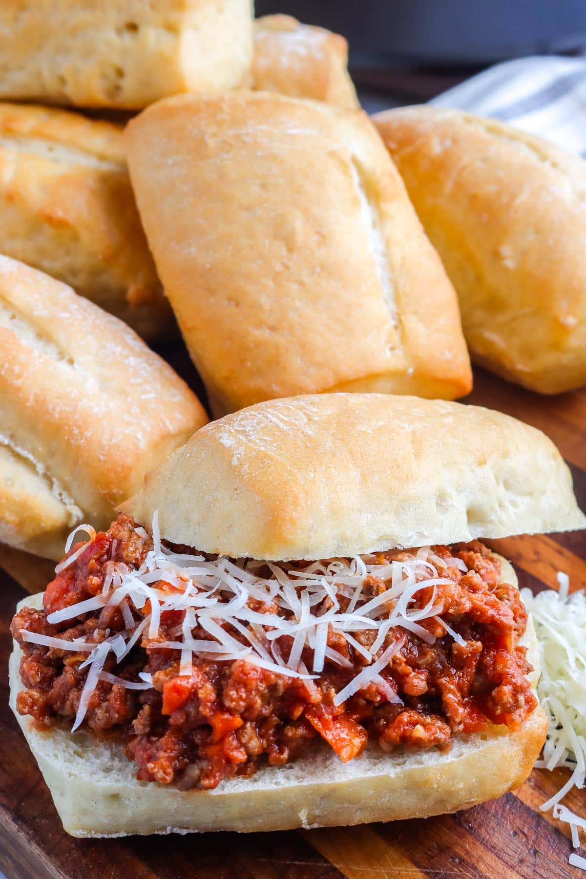 An Italian Sloppy Joe on a cutting board with a pile of ciabatta rolls in the background