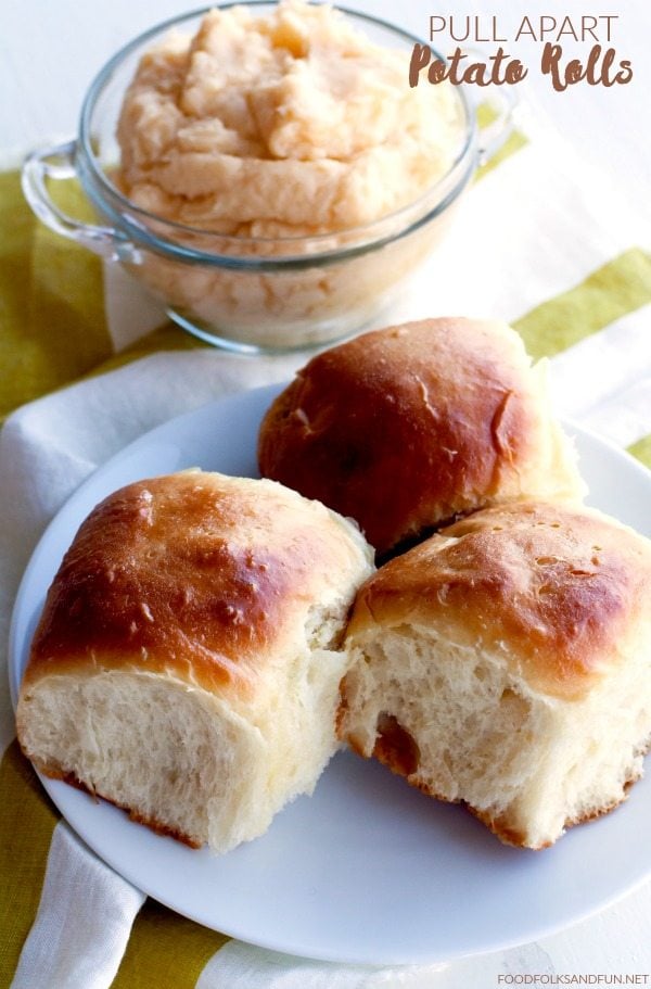 3 potato rolls on a plate with mashed potatoes in the background.