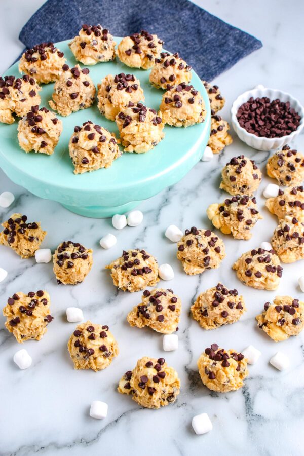 A turquoise cake stand holding no bake avalanche cookies with mini chocolate chips, surrounded by additional cookies and a small bowl of chocolate chips.