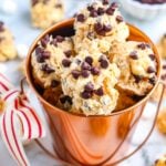 Closeup of avalanche cookies with mini chocolate chips stacked inside a copper bucket with a striped ribbon tied to the handle.
