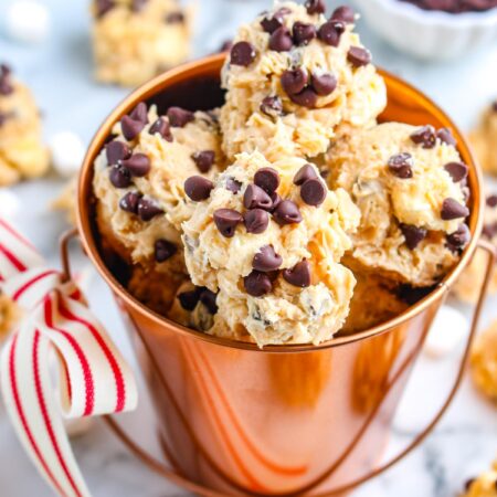 Closeup of avalanche cookies with mini chocolate chips stacked inside a copper bucket with a striped ribbon tied to the handle.