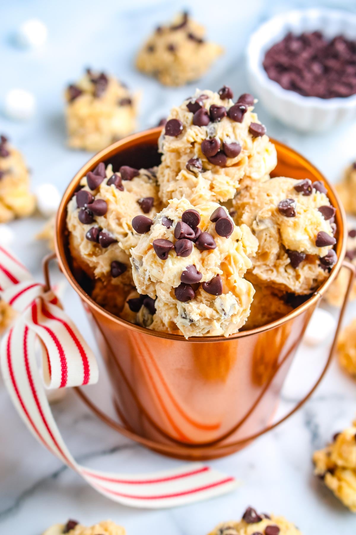 Closeup of avalanche cookies with mini chocolate chips stacked inside a copper bucket with a striped ribbon tied to the handle.