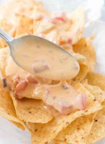 Chile Con Queso being spooned over tortilla chips.