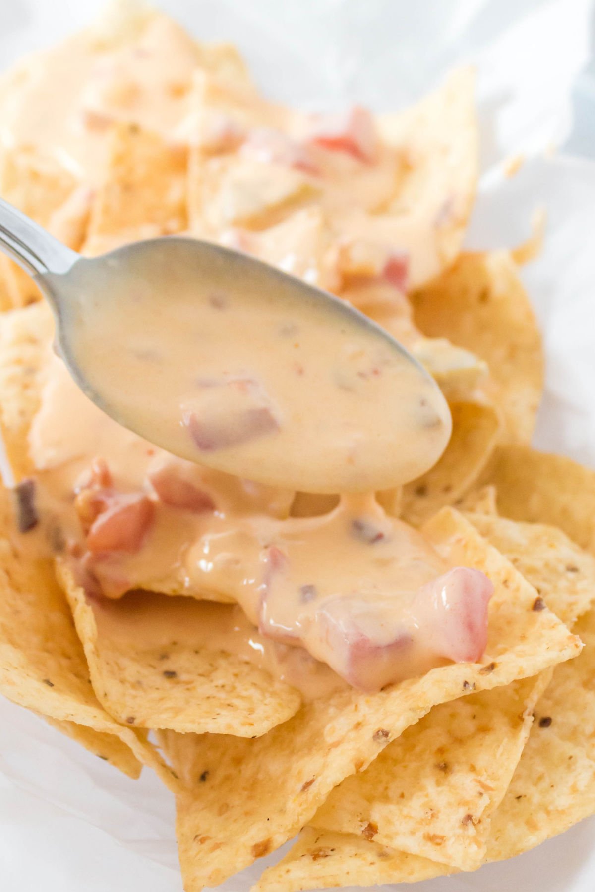 Chile Con Queso being spooned over tortilla chips. 