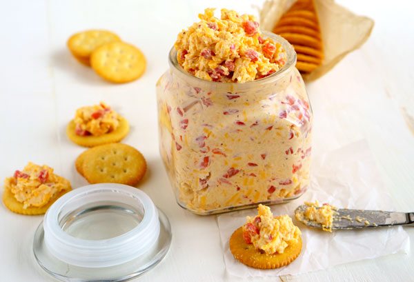 A glass container holding Pimento cheese with crackers on the side for dipping