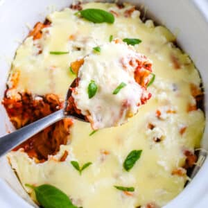 A spoon getting some baked ziti from a crockpot.