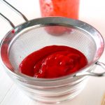 A process shot for straining raspberries for raspberry swirl cheesecake cupcakes