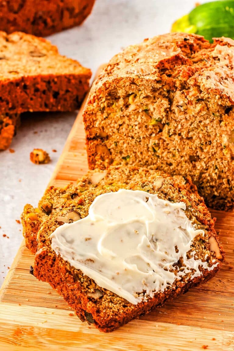 A loaf of moms zucchini bread with a slice cut from it and covered in butter.