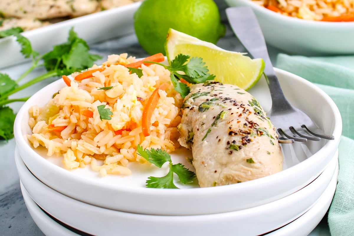 Bowl with cilantro chicken and rice pilaf garnished with fresh cilantro and lime wedges.