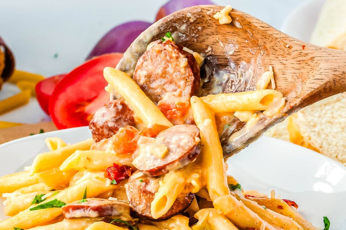 A wooden spoon scooping up the pasta and placing it on the plate.