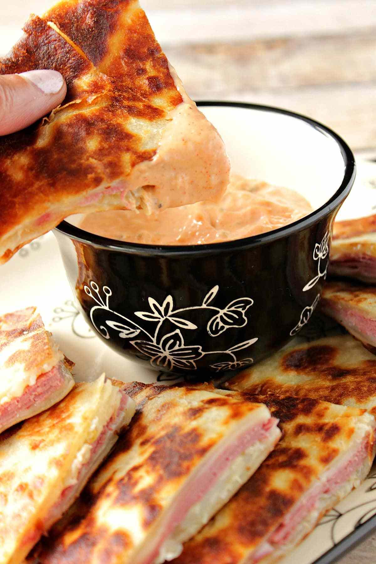 Reuben quesadilla triangles on a serving platter with a bowl of dipping sauce
