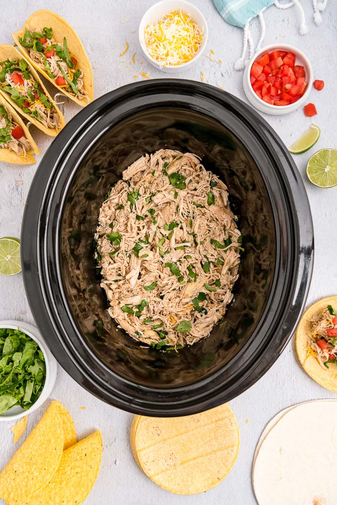An overhead picture of the finished crockpot shredded chicken with all of the fixing to make tacos.