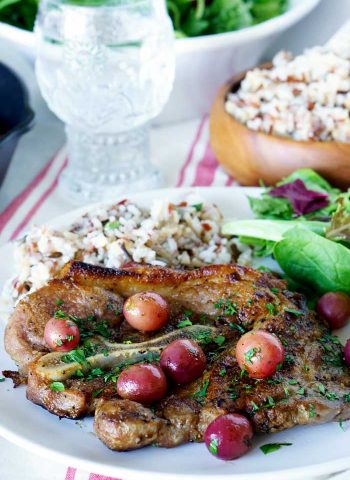 Skillet Pork Chops with grapes and caramelized shallots on a plate with a side salad and rice