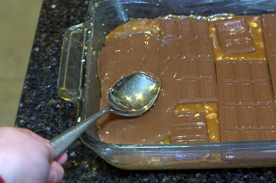 spreading melted chocolate with a spoon in a baking dish