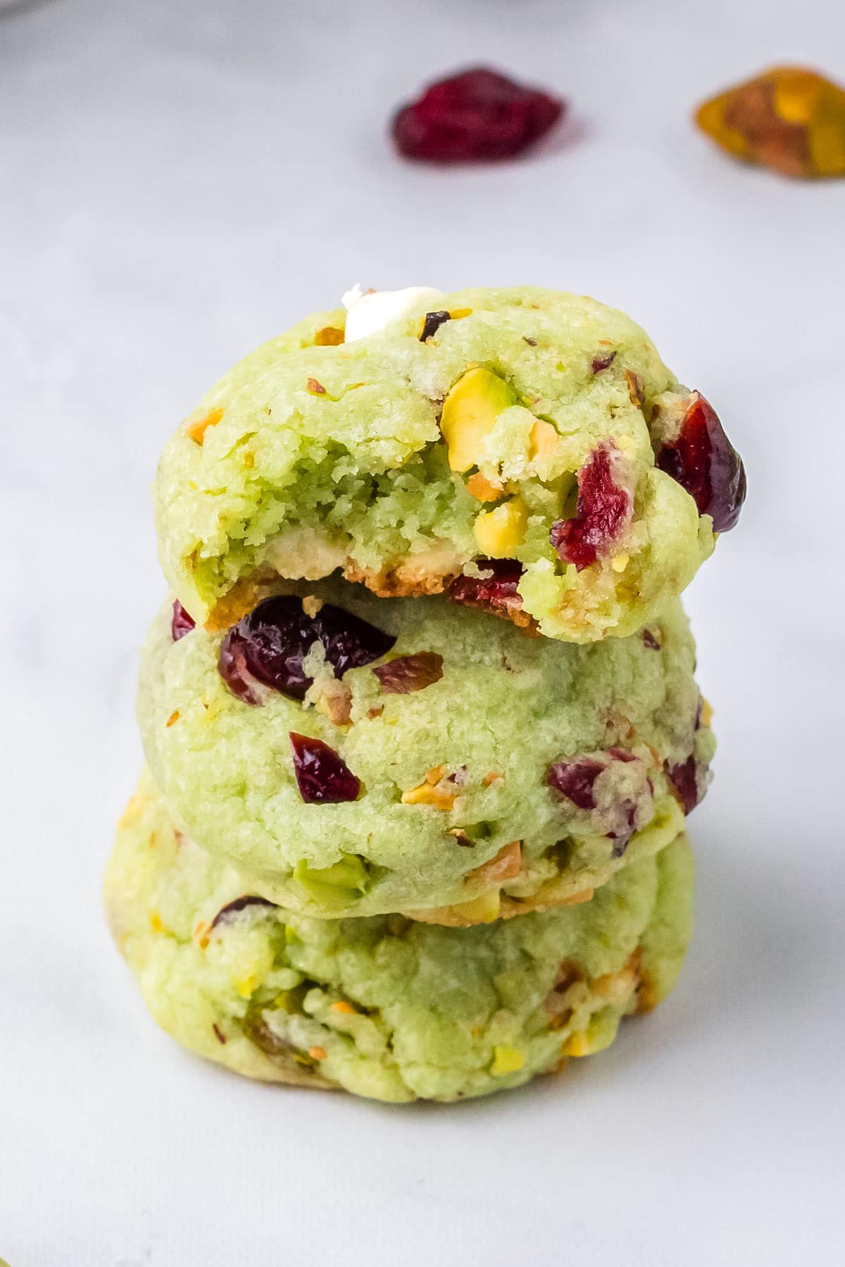 Three Pistachio Cranberry Cookies stacked on top of each other and a bite taken out of the top one so you can see what the interior looks like.