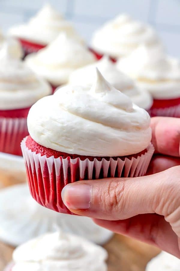 A hand holding a delicious homemade red velvet cupcake.