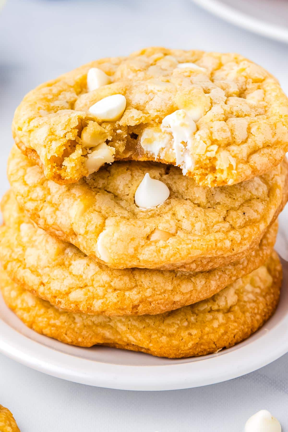 A stack fof 4 brown butter white chocolate macadamia but cookies stacked with a bite taken out of the top on.