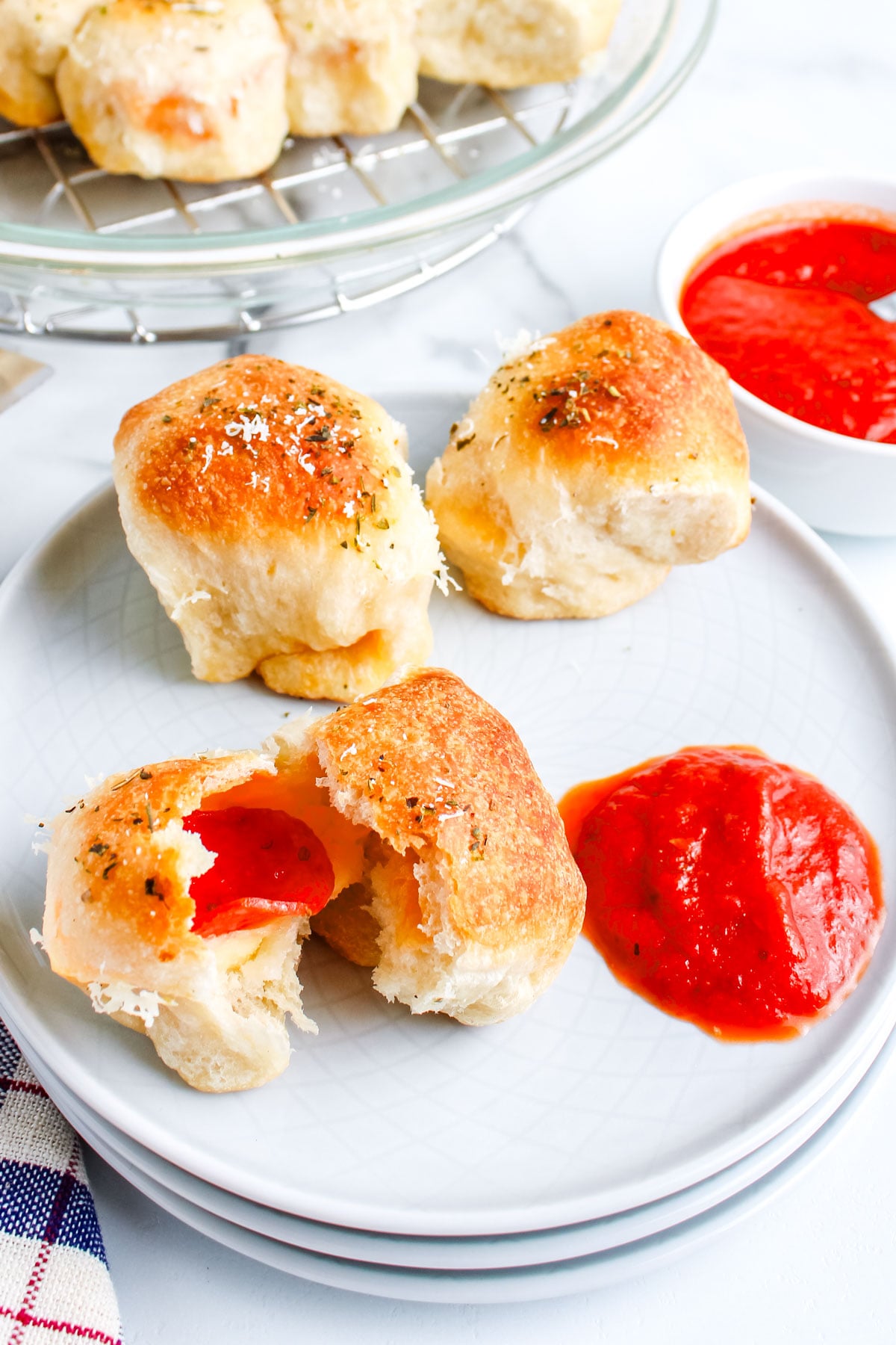 A hand tearing open a warm pizza roll to reveal the melted mozzarella cheese and pepperoni slice inside, with the rest of the batch in the background.