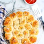 Pull apart pepperoni pizza rolls baked until golden and served in a round glass dish with pizza sauce nearby.