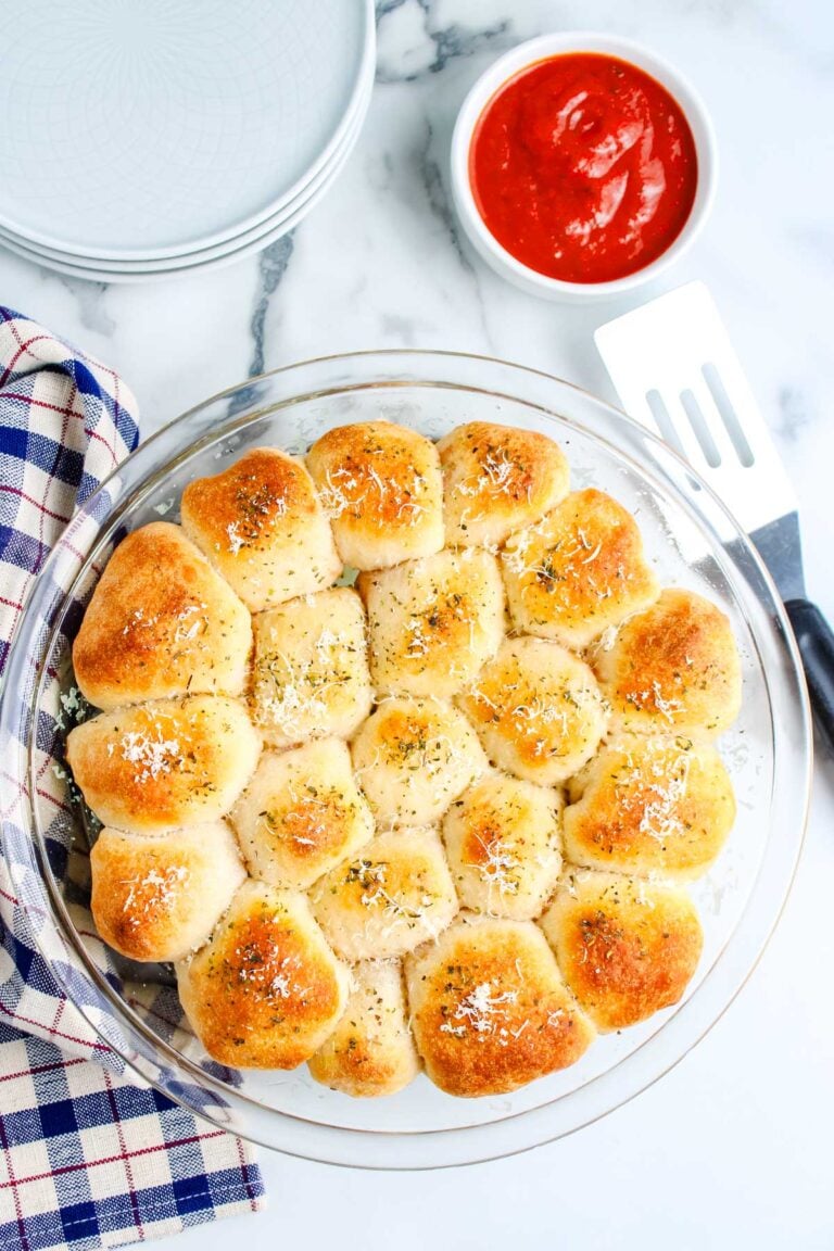 Pull apart pepperoni pizza rolls baked until golden and served in a round glass dish with pizza sauce nearby.