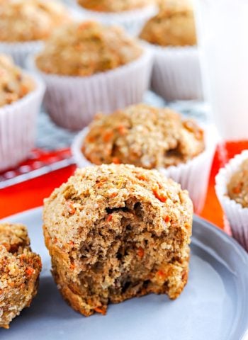 A close up of carrot muffins, one with a bite taken out of it so you can see the interior.