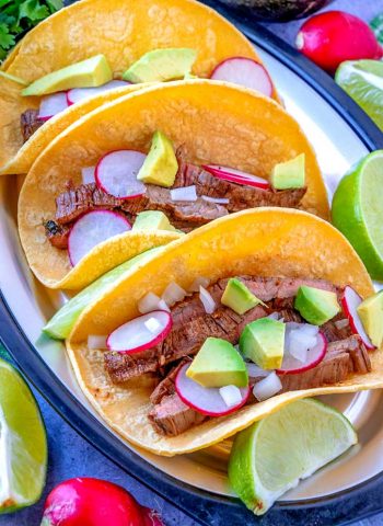 3 Carne Asada Street Tacos on a plate with radishes, chopped onions, and avocado.