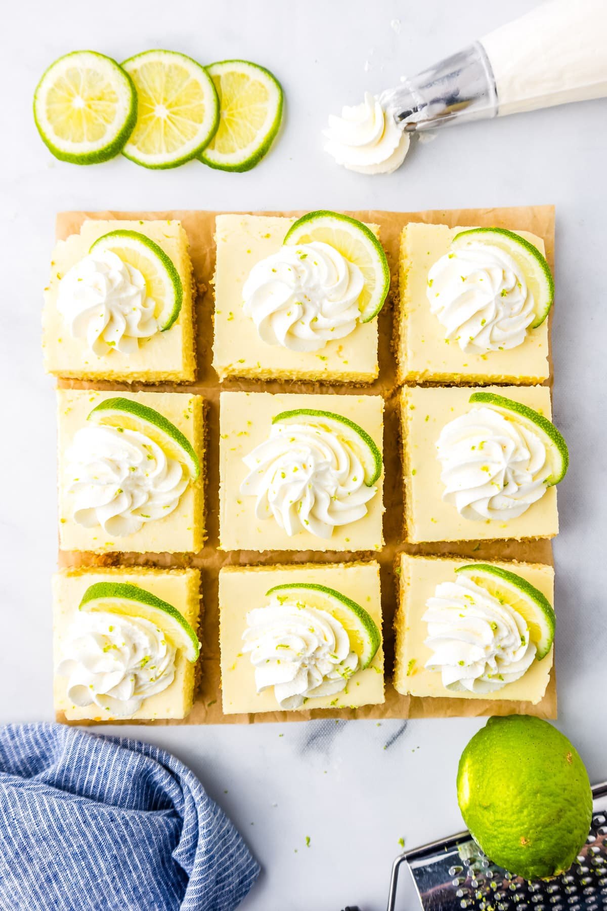 An overhead picture of nine Key Lime Pie Bars cut on a tabletop and garnished with whipped cream. 