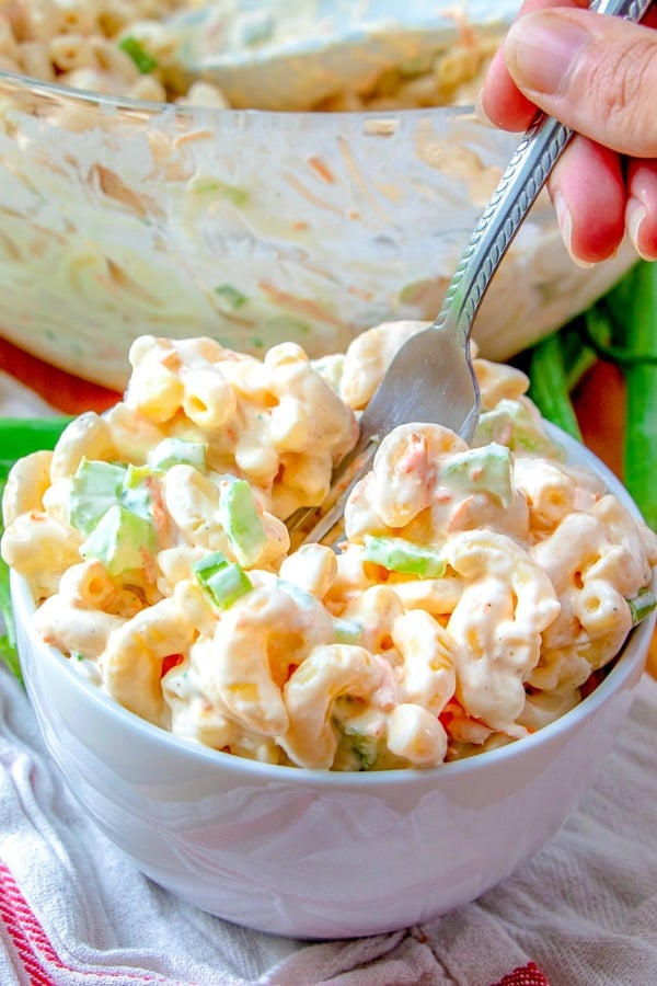 Mac salad in a white bowl with a fork digging into the salad.