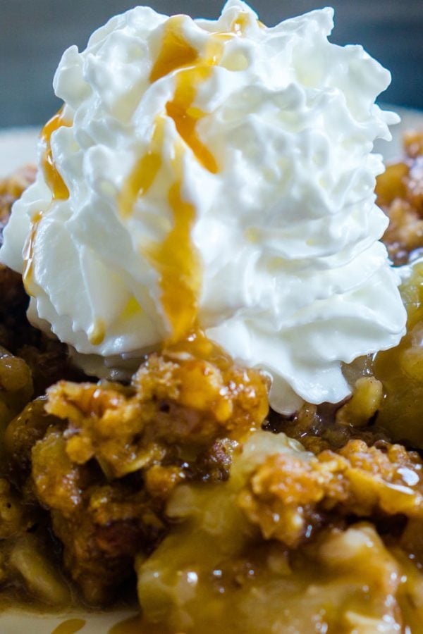A close up picture of apple crisp with whipped cream and caramel sauce.