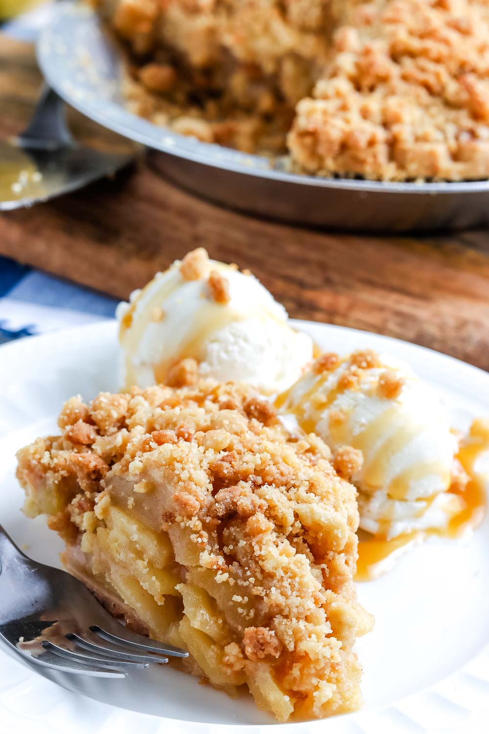 A slice of Dutch Apple Pie on a white plate with two scoops of vanilla ice cream.