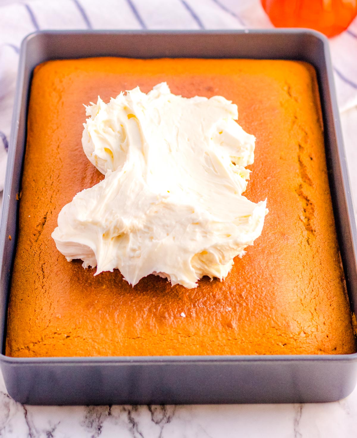 Freshly baked pumpkin snack cake in a pan with a large scoop of cream cheese frosting on top, ready to be spread.