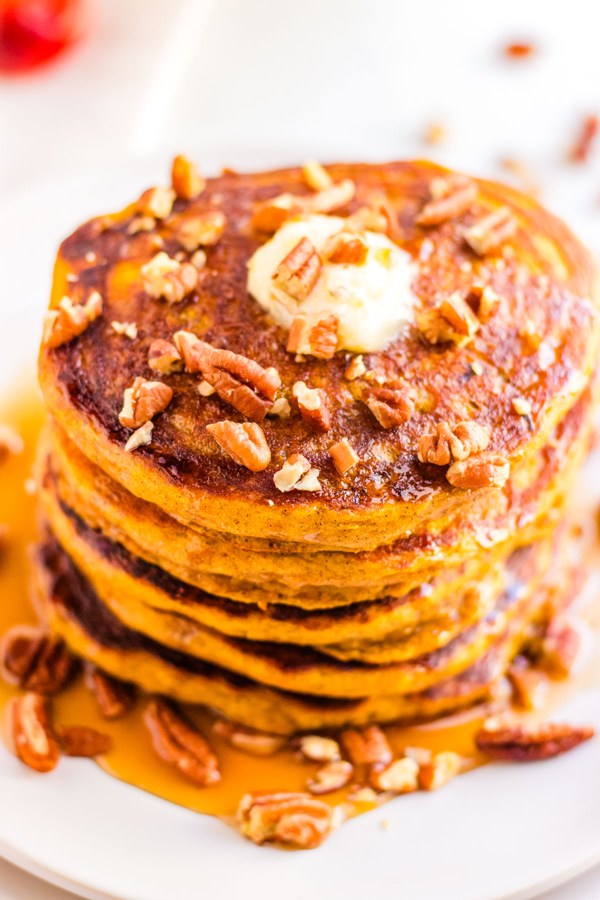 Stack of fluffy pumpkin pie spice pancakes topped with butter, chopped pecans, and maple syrup for a cozy fall breakfast.