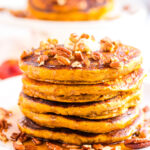 Close-up of pumpkin spice pancakes made with buttermilk, served with maple syrup, butter, and toasted pecans.