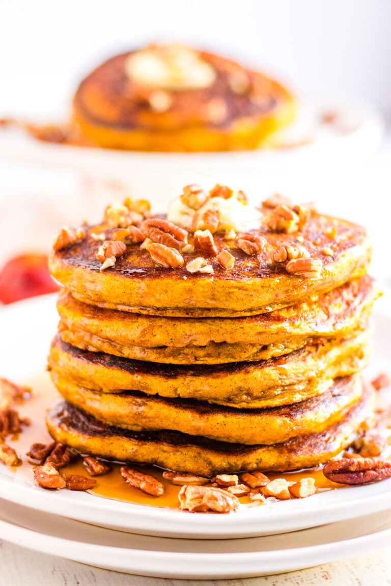 Close-up of pumpkin spice pancakes made with buttermilk, served with maple syrup, butter, and toasted pecans.