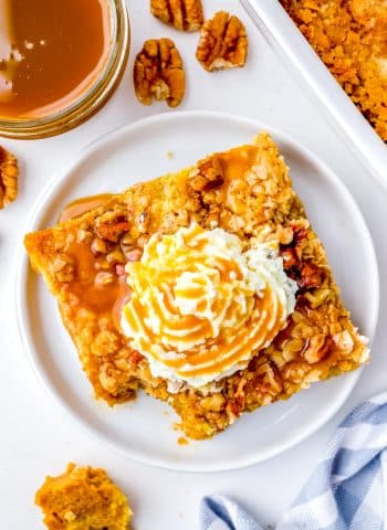 An overhead picture of the finished Pumpkin Dump Cake on a white plate garnished with whipped cream and caramel sauce.