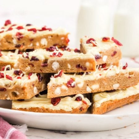 Sliced cranberry bliss bars stacked on top of each other on a white platter.