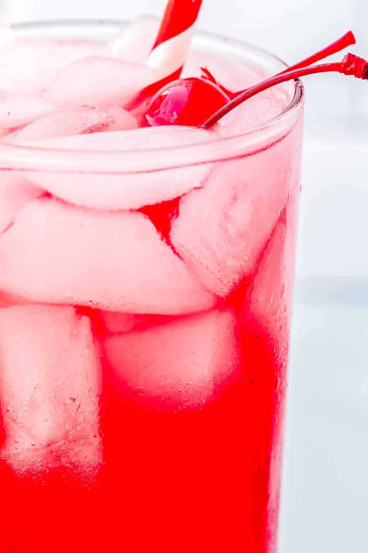 A close up of a glass of a red cocktail garnished with a cherry.