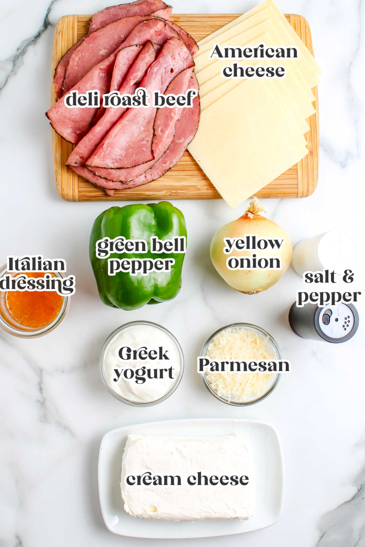 A flat lay of the ingredients needed for the dip, including deli roast beef, American cheese slices, green bell pepper, yellow onion, cream cheese, Greek yogurt, parmesan, and a jar of Italian dressing.