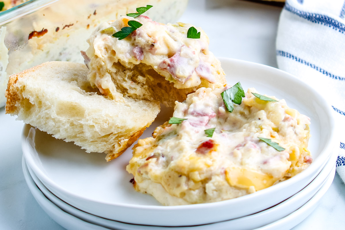 A close-up view of creamy Philly Cheesesteak Dip piled high on two slices of soft French bread, showing the texture of the roast beef and peppers.