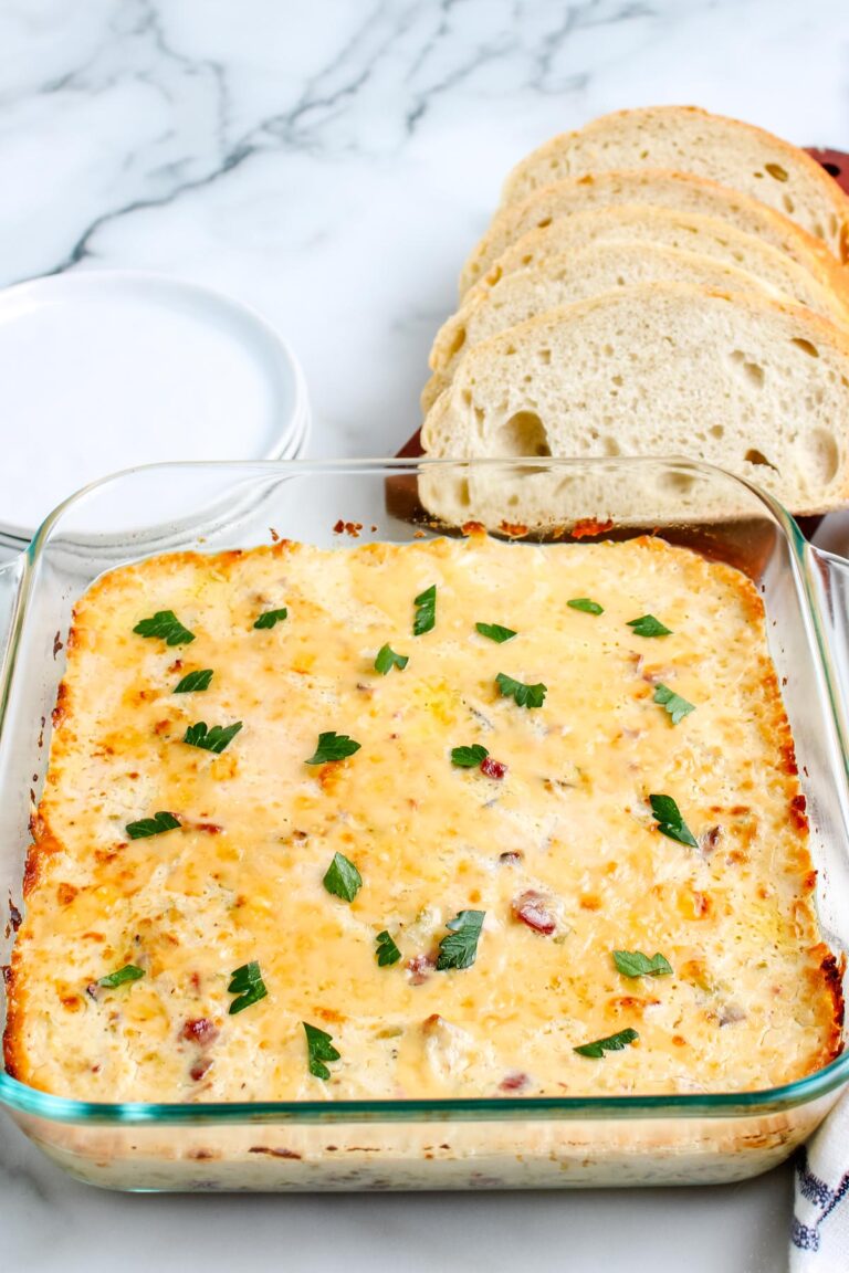 An overhead view of the baked Philly Cheesesteak Dip in a glass dish, garnished with fresh parsley and served with a side of sliced baguette for dipping.