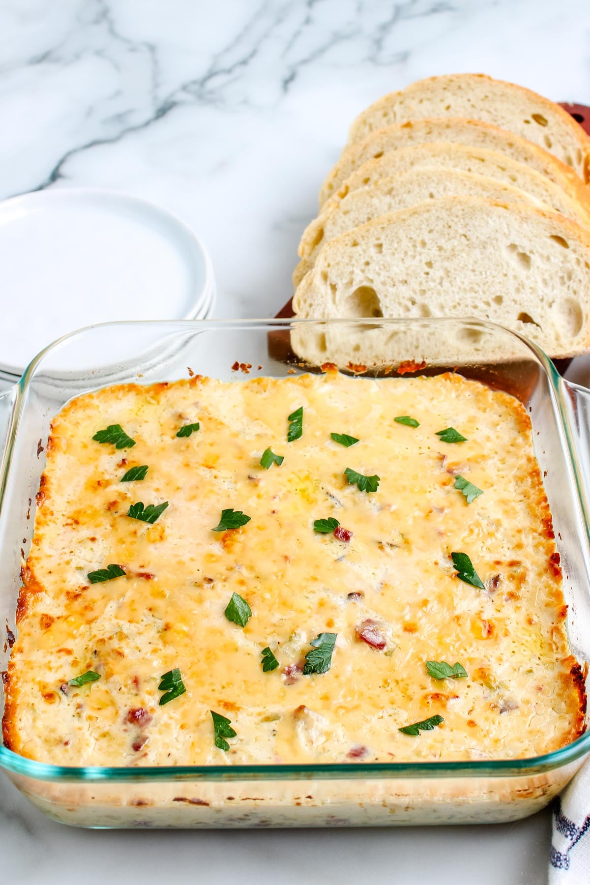 An overhead view of the baked Philly Cheesesteak Dip in a glass dish, garnished with fresh parsley and served with a side of sliced baguette for dipping.